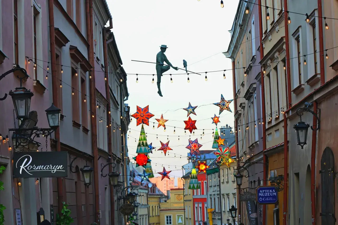 Lublin trasa: rzeźba akrobaty na linie, kolorowe gwiazdy i lampki nad ulicą Stare Miasto.