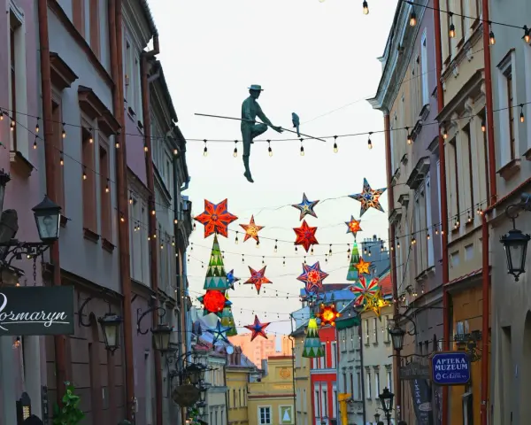 Lublin trasa: rzeźba akrobaty na linie, kolorowe gwiazdy i lampki nad ulicą Stare Miasto.