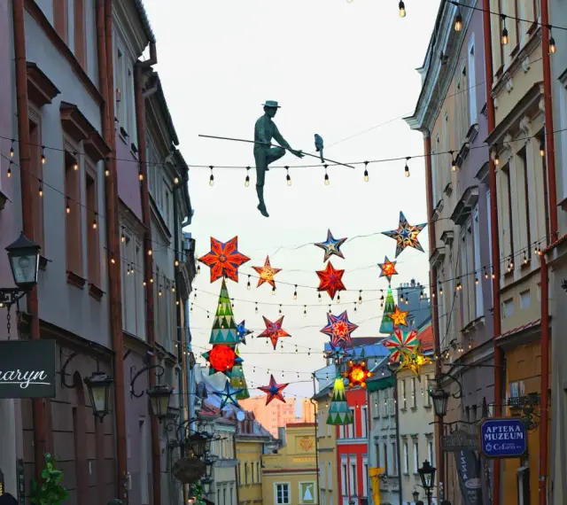 Lublin trasa: rzeźba akrobaty na linie, kolorowe gwiazdy i lampki nad ulicą Stare Miasto.