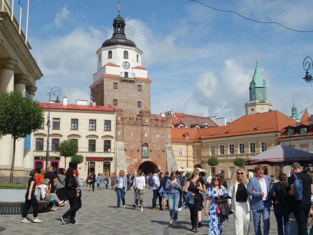 Ludzie spacerują po Rynku Starego Miasta w Lublinie, mijając Bramę Krakowską. To popularna lublin trasa turystyczna.