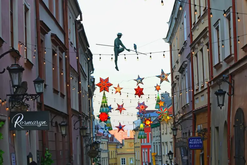 Lublin trasa: rzeźba akrobaty na linie, kolorowe gwiazdy i lampki nad ulicą Stare Miasto.